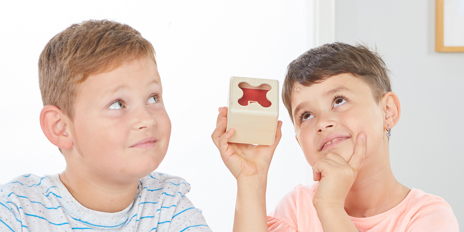 Zwei Kinder konzentrieren sich auf das Geräusch, das entsteht, wenn der Akustikwürfel gedreht wird.