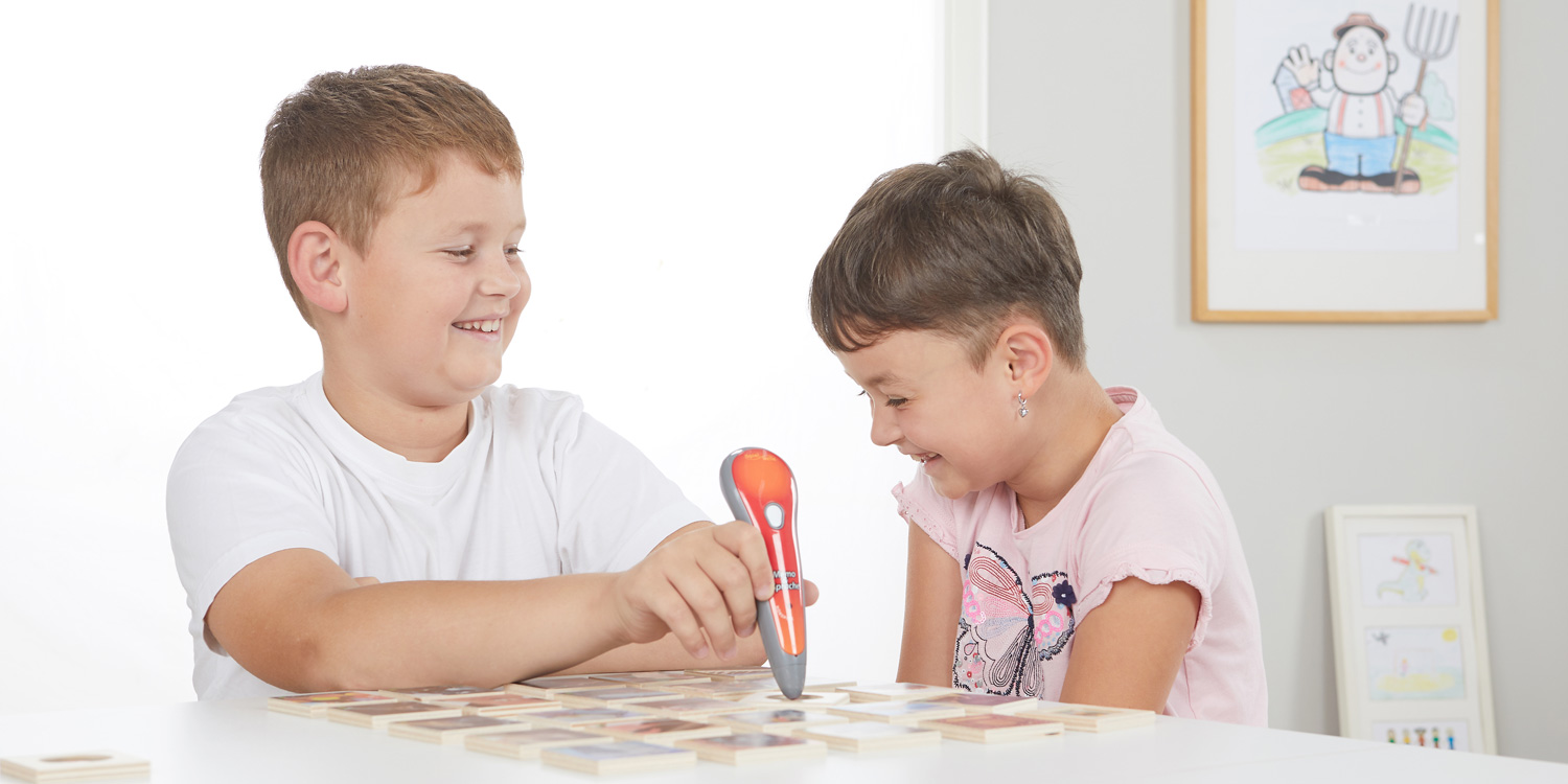 Beim Spielen mit HÖRspitz haben zwei Kinder viel Spaß. Ein Junge spielt Geräusche mit dem Stift ab und ein Mädchen lacht beim Zuhören.