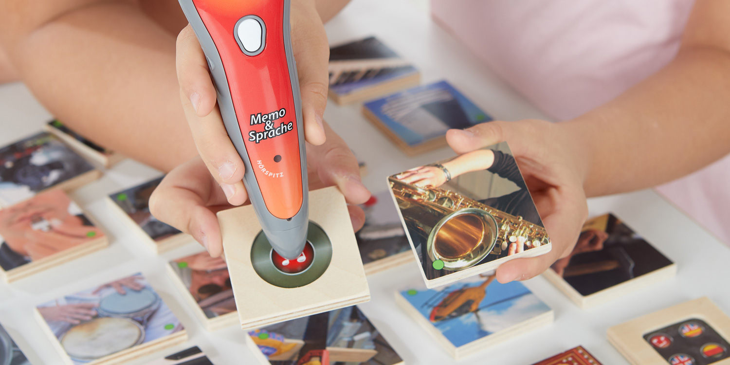 Der Stift spielt links im Bild ein Geräusch von der Rückseite der Holztafel. Die passende Bildtafel zeigt ein Saxofon auf der rechten Seite.