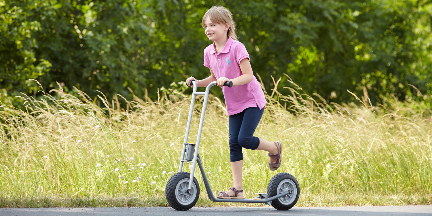 Mädchen fährt draußen mit dem Spielwelle Roller L